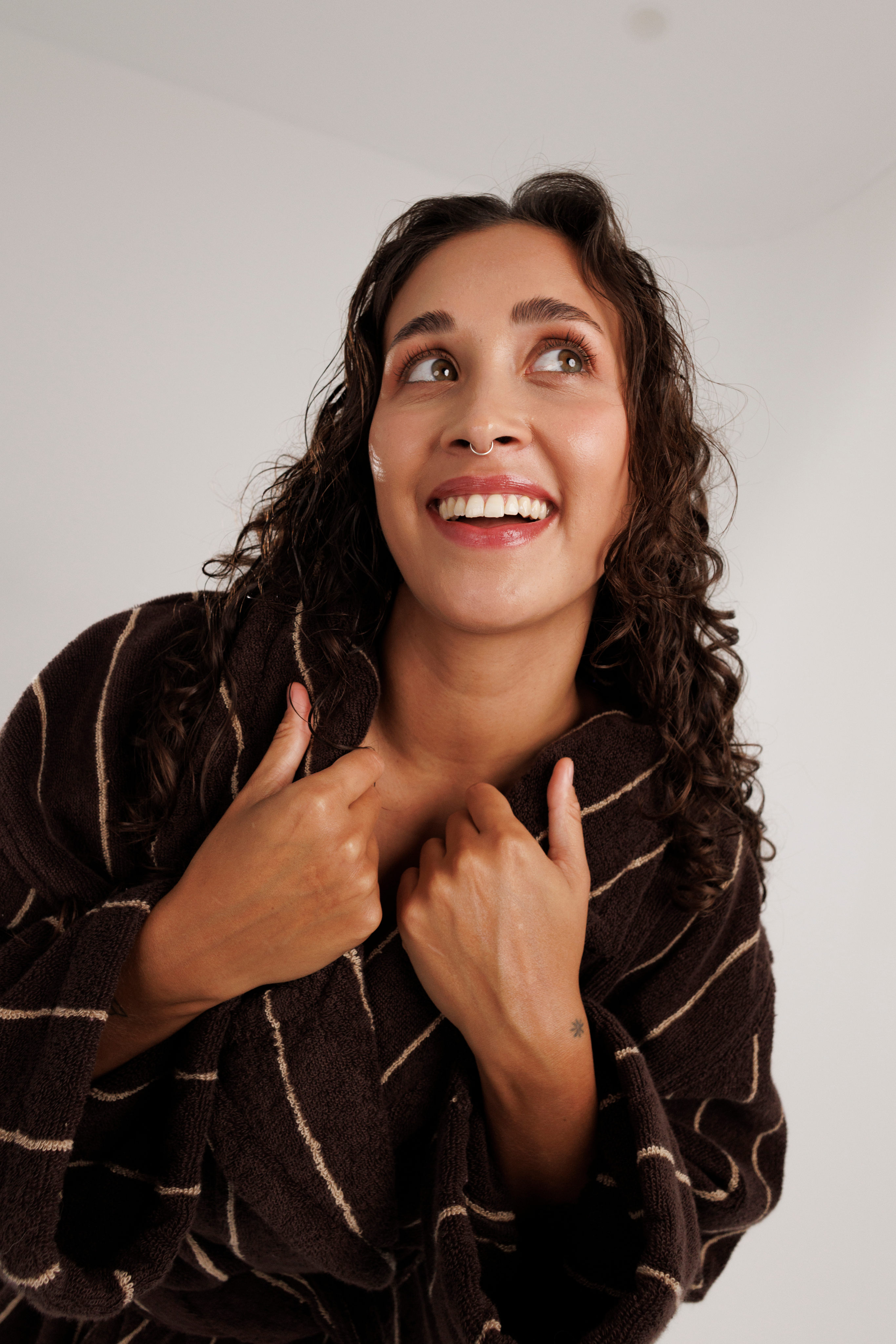 Woman with curly hair smiling and looking up, wearing a brown striped robe.